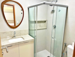 A bathroom with a glass-enclosed shower, a sink with a mirror, and a toilet. - Vacanze - Ipioca Beach (Maceió)