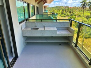 Un balcón moderno con un lavamanos integrado y barandilla de vidrio con vista a un paisaje exuberante.