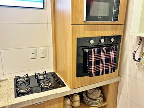 A kitchen with a gas stove, oven, and a microwave above it. - Vacanze - Ipioca Beach (Maceió)