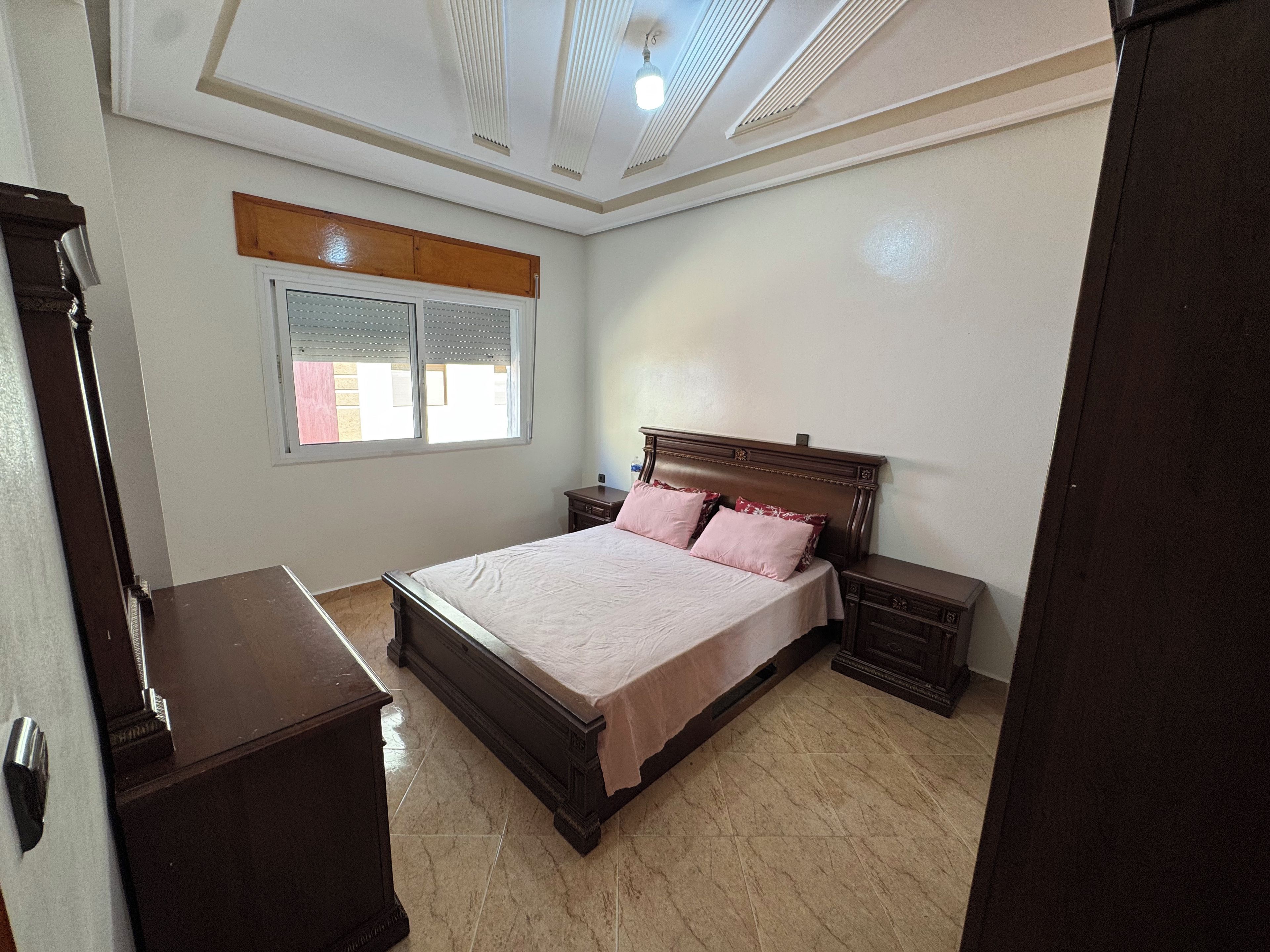 A bedroom with a large bed, a nightstand, a dresser, and a window with blinds.