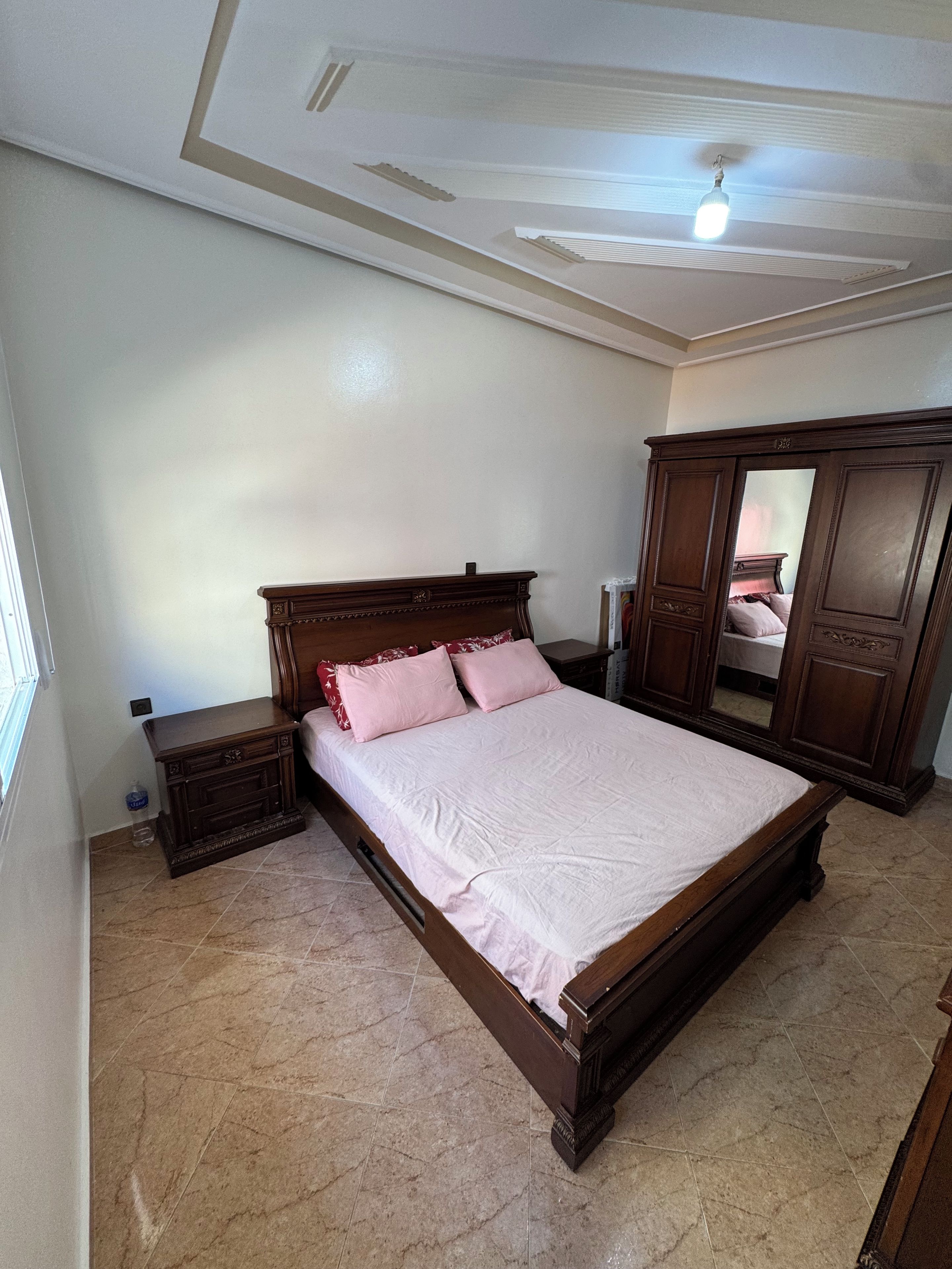 Une chambre avec un grand lit, une armoire et un ventilateur de plafond.