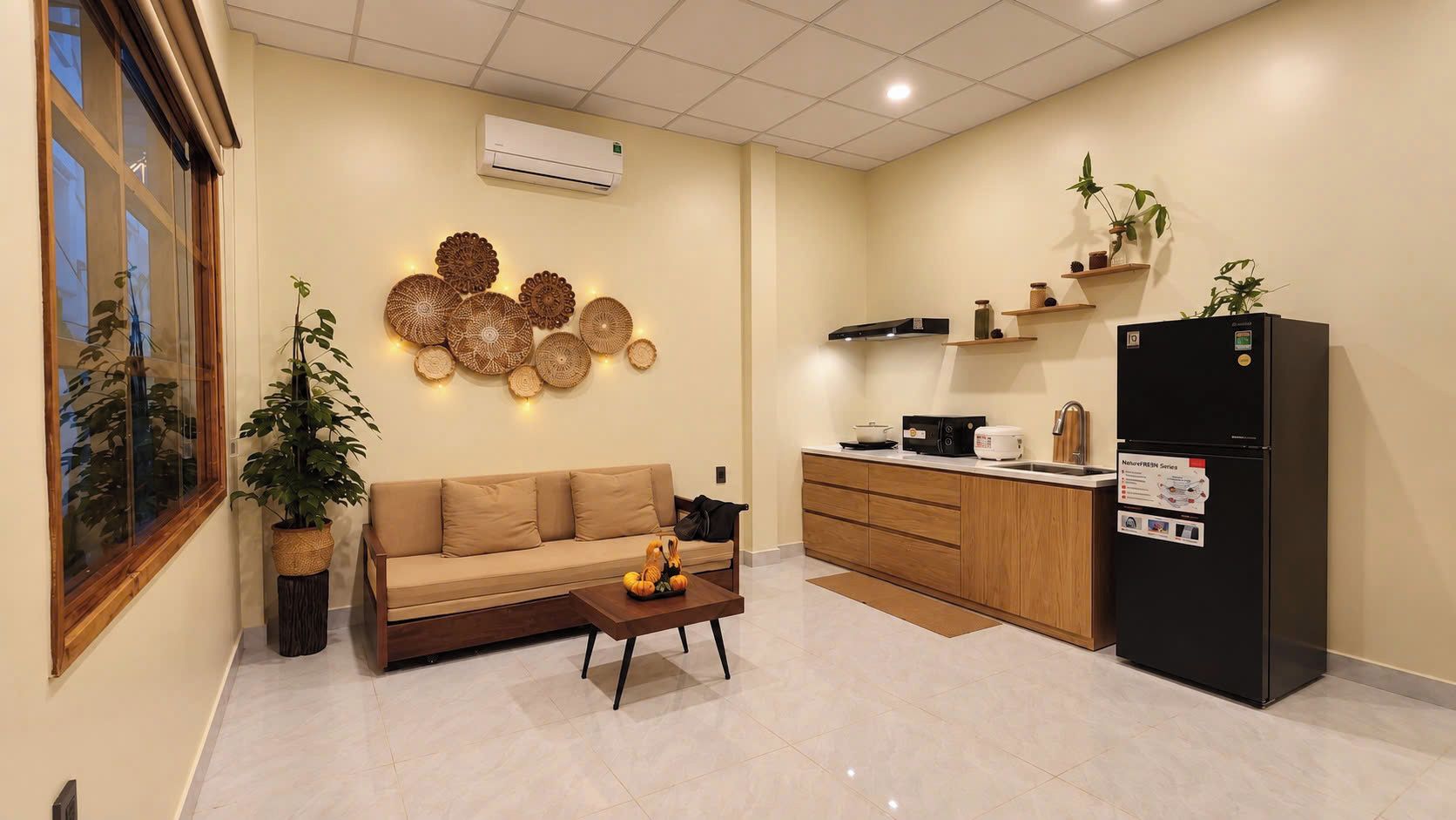 A modern kitchen with a black refrigerator, wooden cabinets, and a beige sofa in a living area.