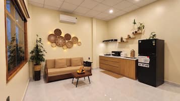 A modern kitchen with a black refrigerator, wooden cabinets, and a beige sofa in a living area.