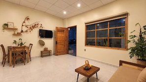 Una sala de estar con comedor, una puerta de madera, un ventanal grande y un televisor en la pared.