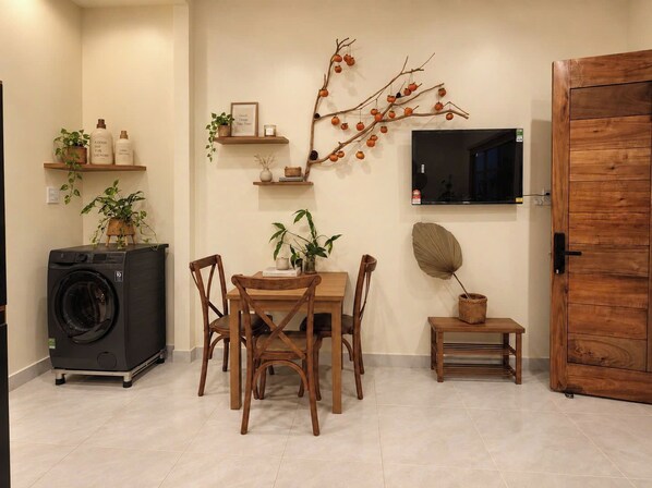 Un espacio habitable funcional con una mesa de comedor, sillas, lavadora, televisor y decoración mural.