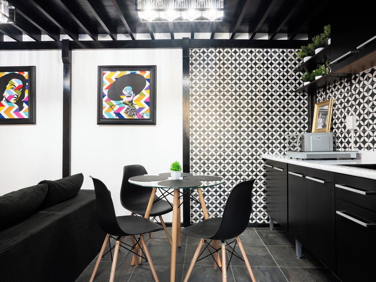 Eine moderne Küche mit einer schwarz-weißen Spritzschutzwand, ein Essbereich mit rundem Tisch und Stühlen sowie eine schwarze Couch mit Kissen.