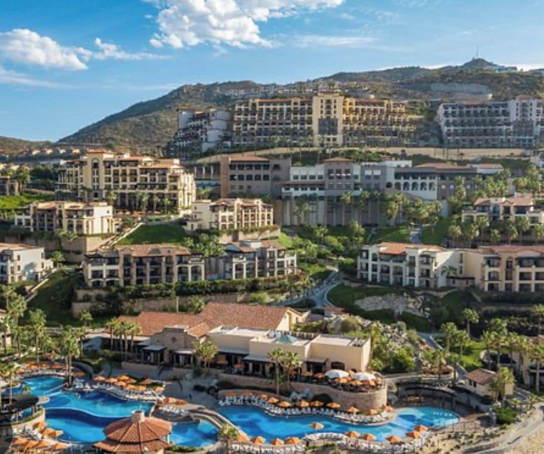 A resort with multiple buildings, a central pool area, and a mountainous backdrop.