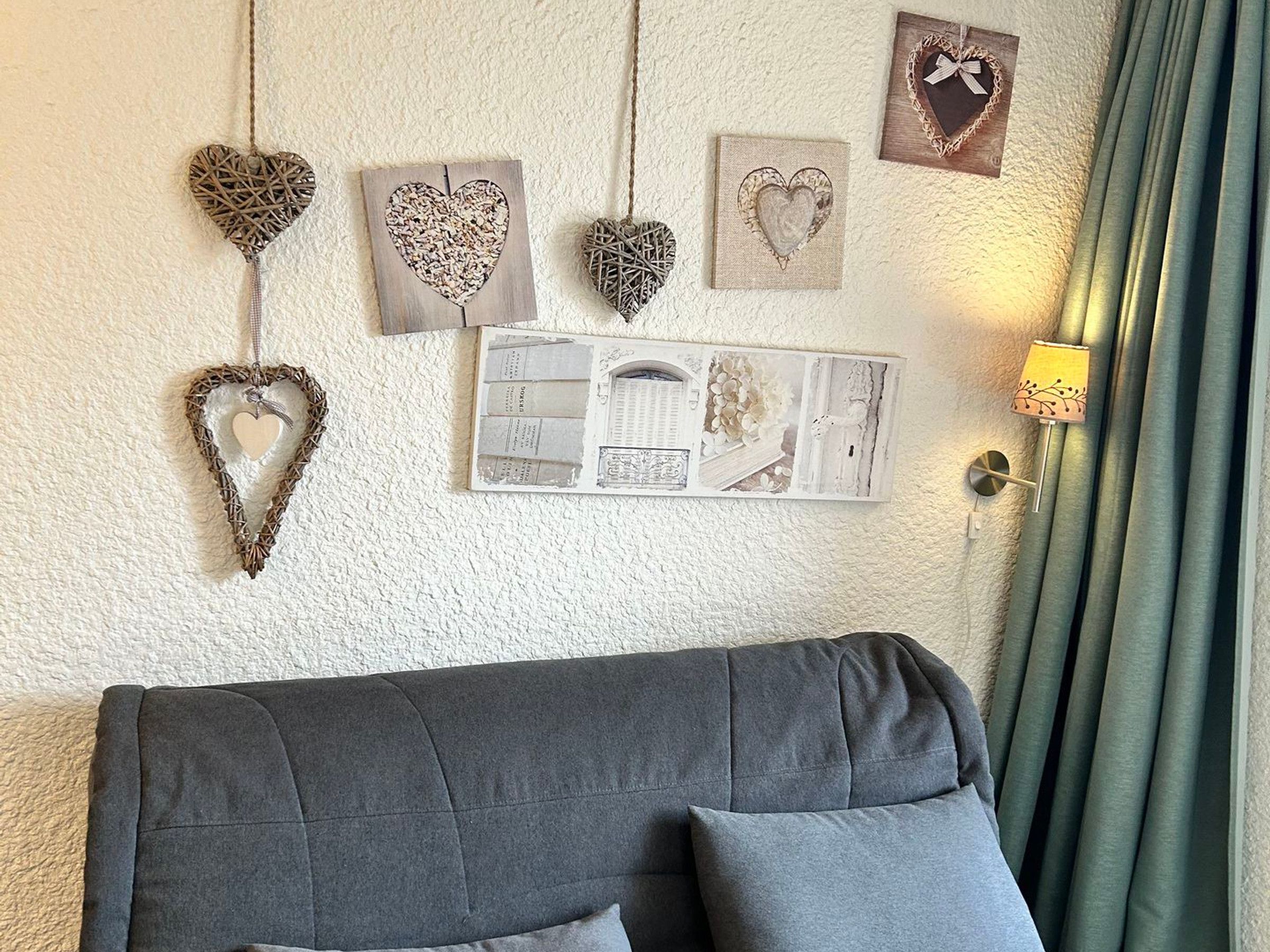 Une pièce avec un canapé gris, des décorations murales en forme de cœur et un tableau encadré.