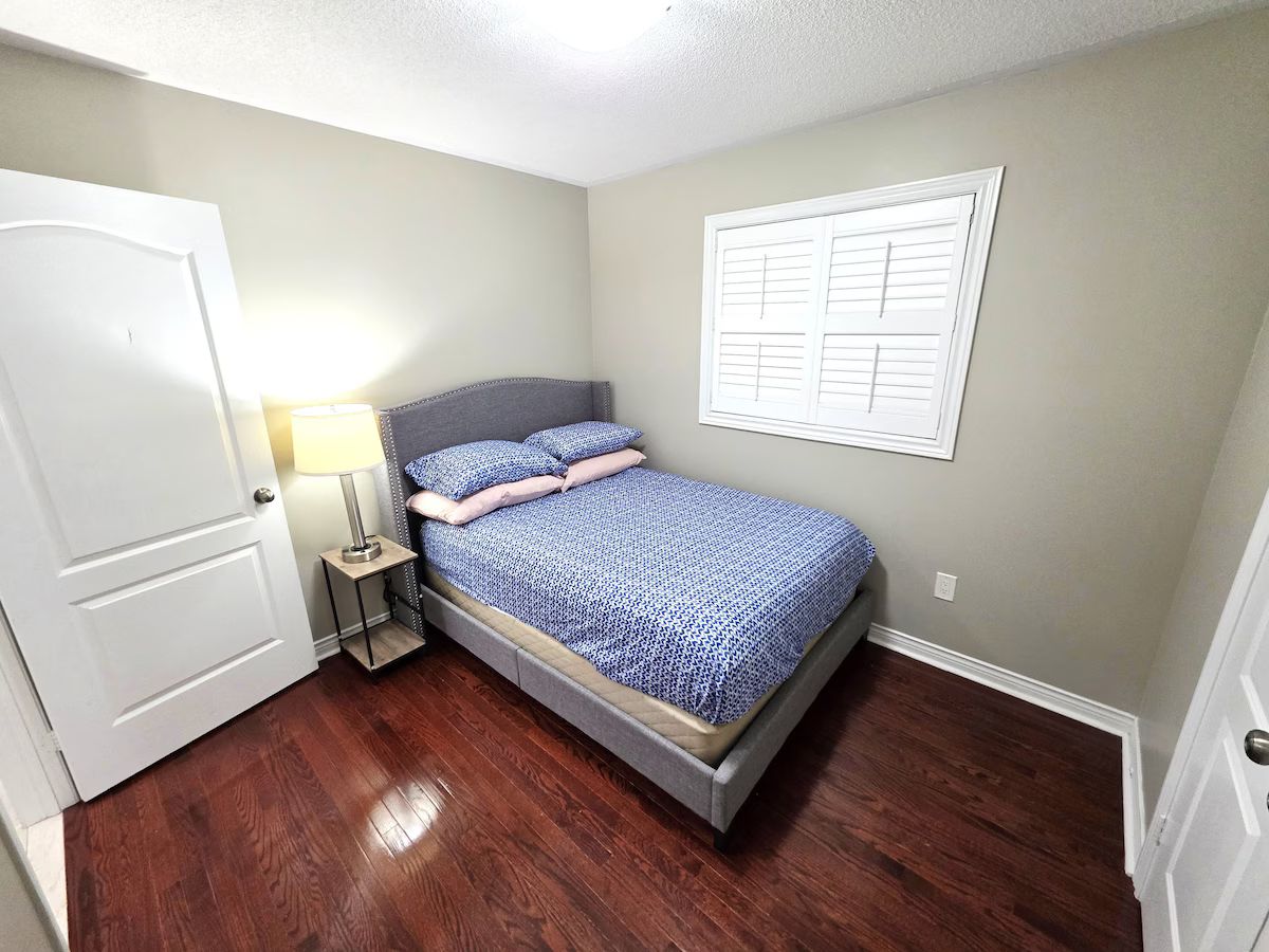 A bedroom with a bed, nightstand, and a window with blinds.