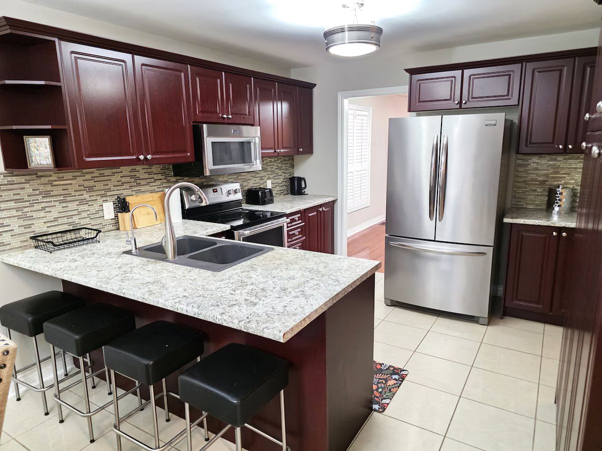 A kitchen with dark wood cabinets, a stainless steel refrigerator, a microwave, and a granite countertop.