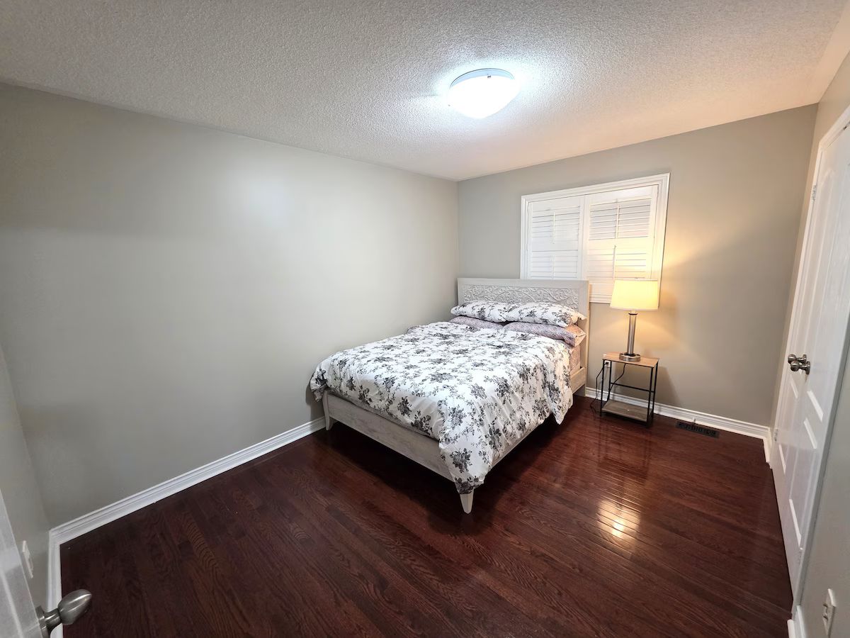 A bedroom with a bed, a nightstand, a lamp, and a door.