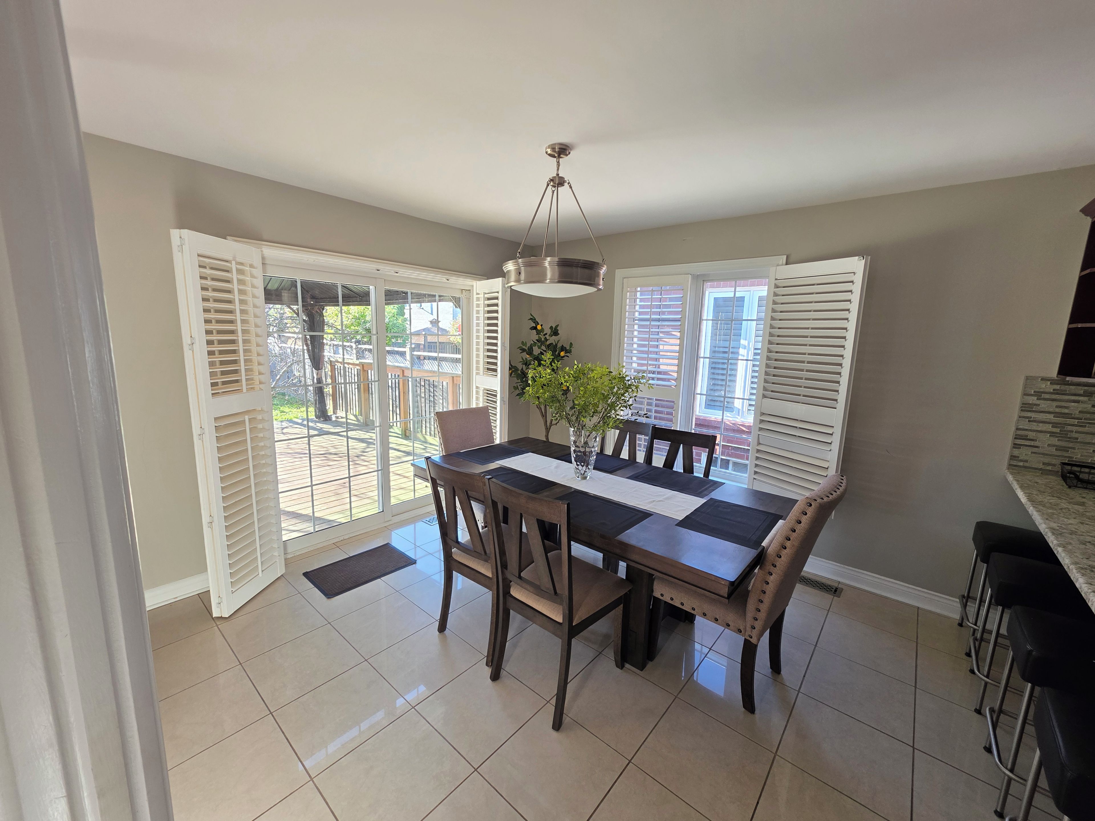 A dining area with a table, chairs, a vase with flowers, and a view through a glass door to an outdoor deck.