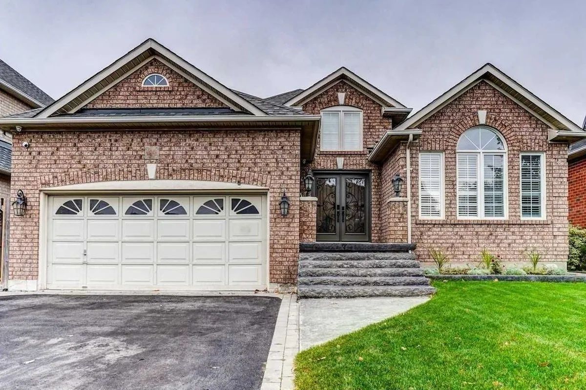 A two-story brick house with a white garage door, a front entrance with steps, and a small front yard.