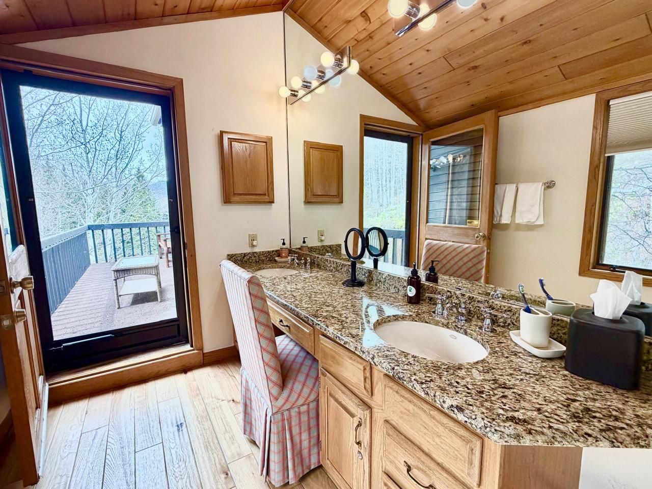 A bathroom with a large sink, wooden cabinets, a mirror, and a view of a deck.