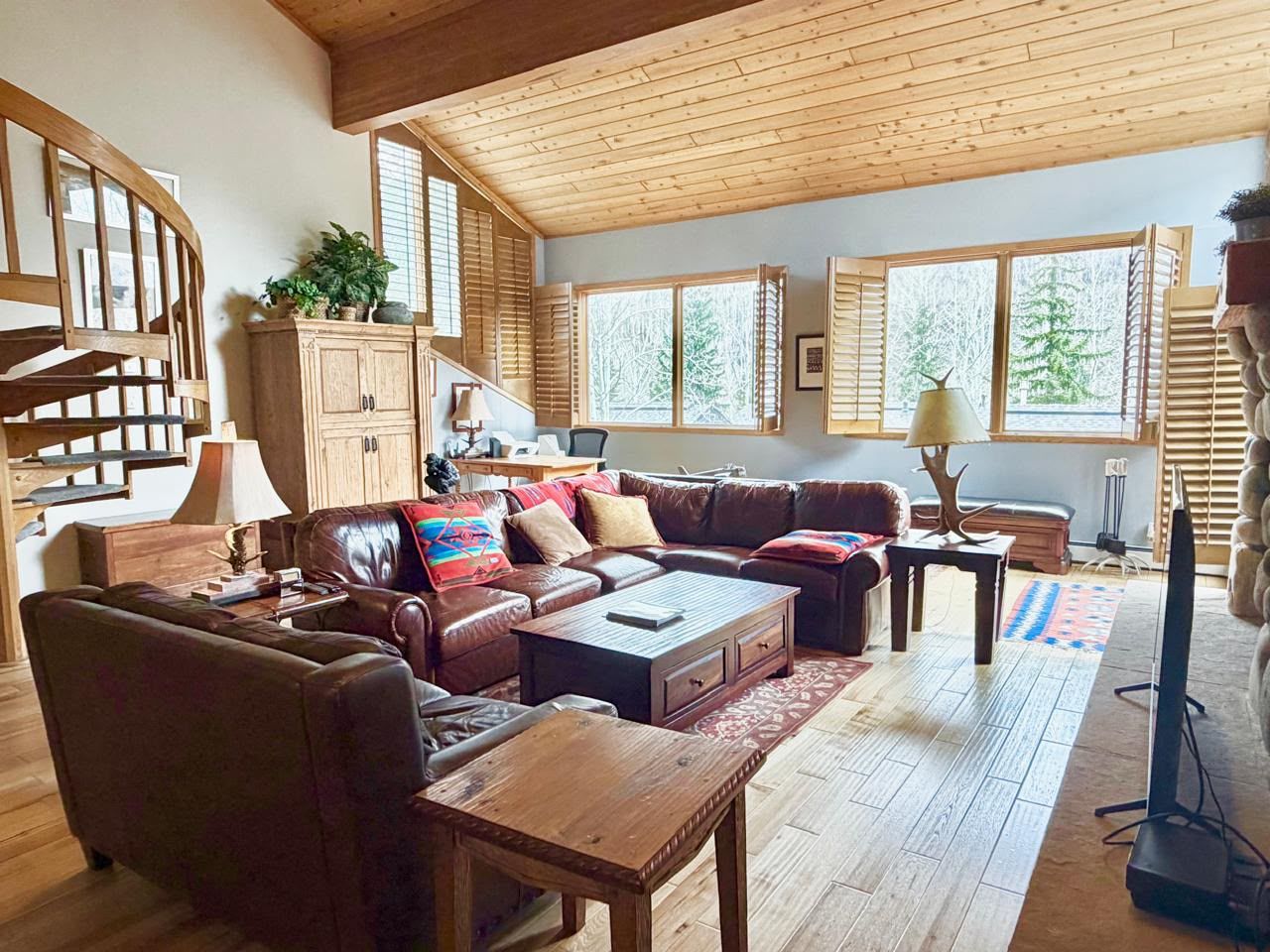 Un salon spacieux avec un plafond en bois, un canapé en cuir marron, une table basse en bois et un téléviseur.