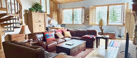 A spacious living room with a wooden ceiling, a brown leather sofa, a wooden coffee table, and a television.