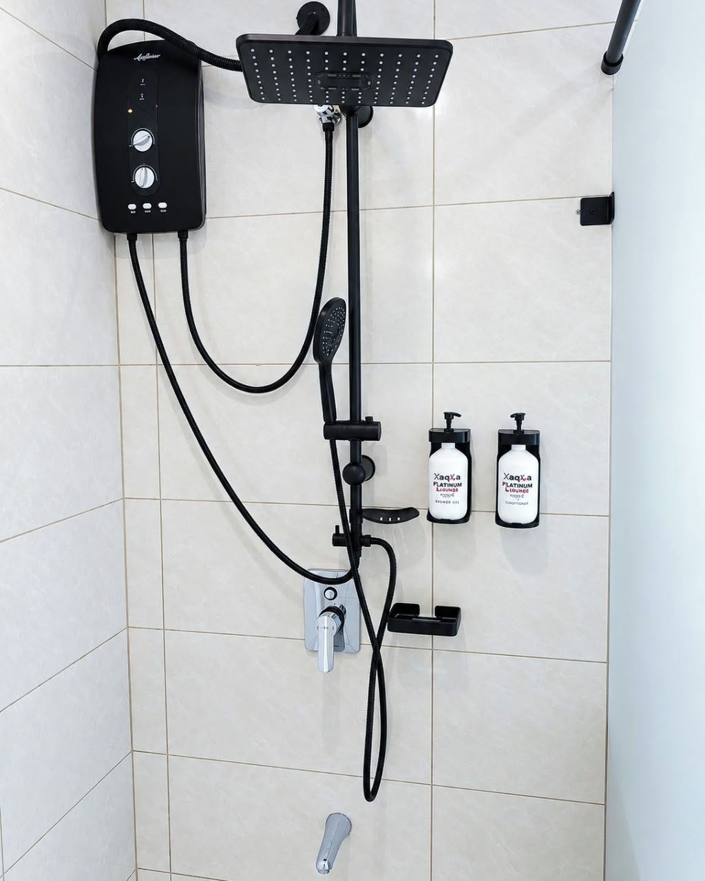 A shower with a handheld showerhead, a wall-mounted control panel, and two bottles of shampoo.
