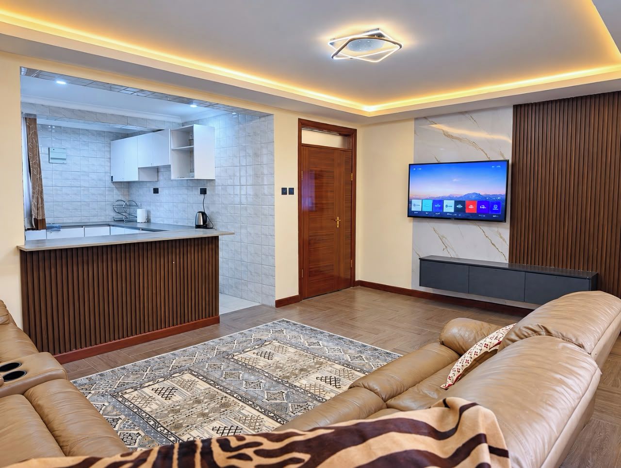 Una sala moderna con un sofá, un televisor y una cocina visible a través de una puerta abierta.