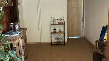 Une pièce avec un plancher en bois, un plafond blanc, une étagère remplie de livres et de bocaux, une plante et une porte qui donne sur une autre pièce.