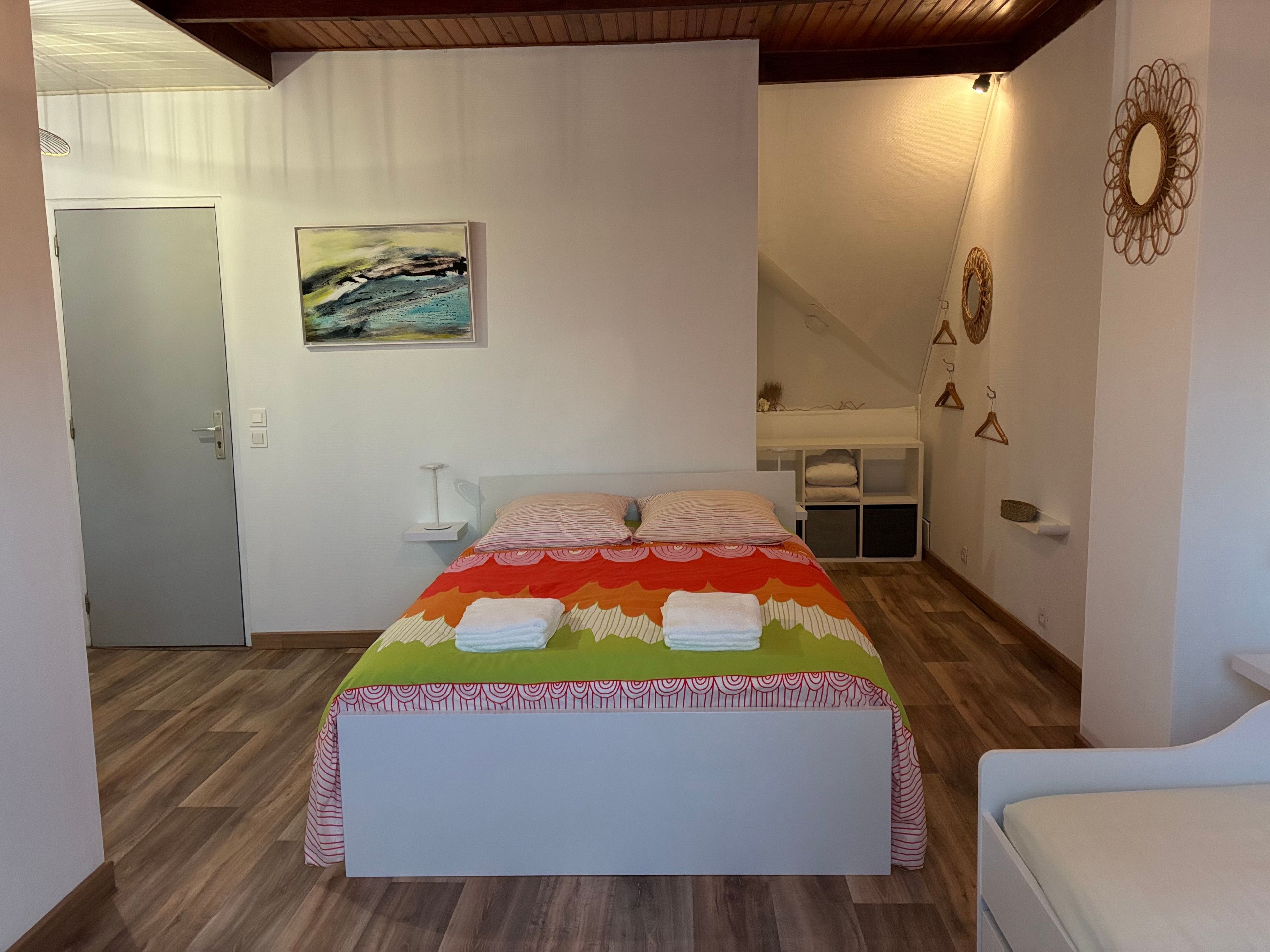 Une chambre à coucher avec un lit, un tableau, une table de chevet blanche et un luminaire suspendu.