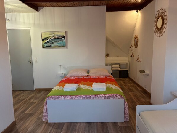 A bedroom with a bed, a painting, a white bedside table, and a hanging light fixture.
