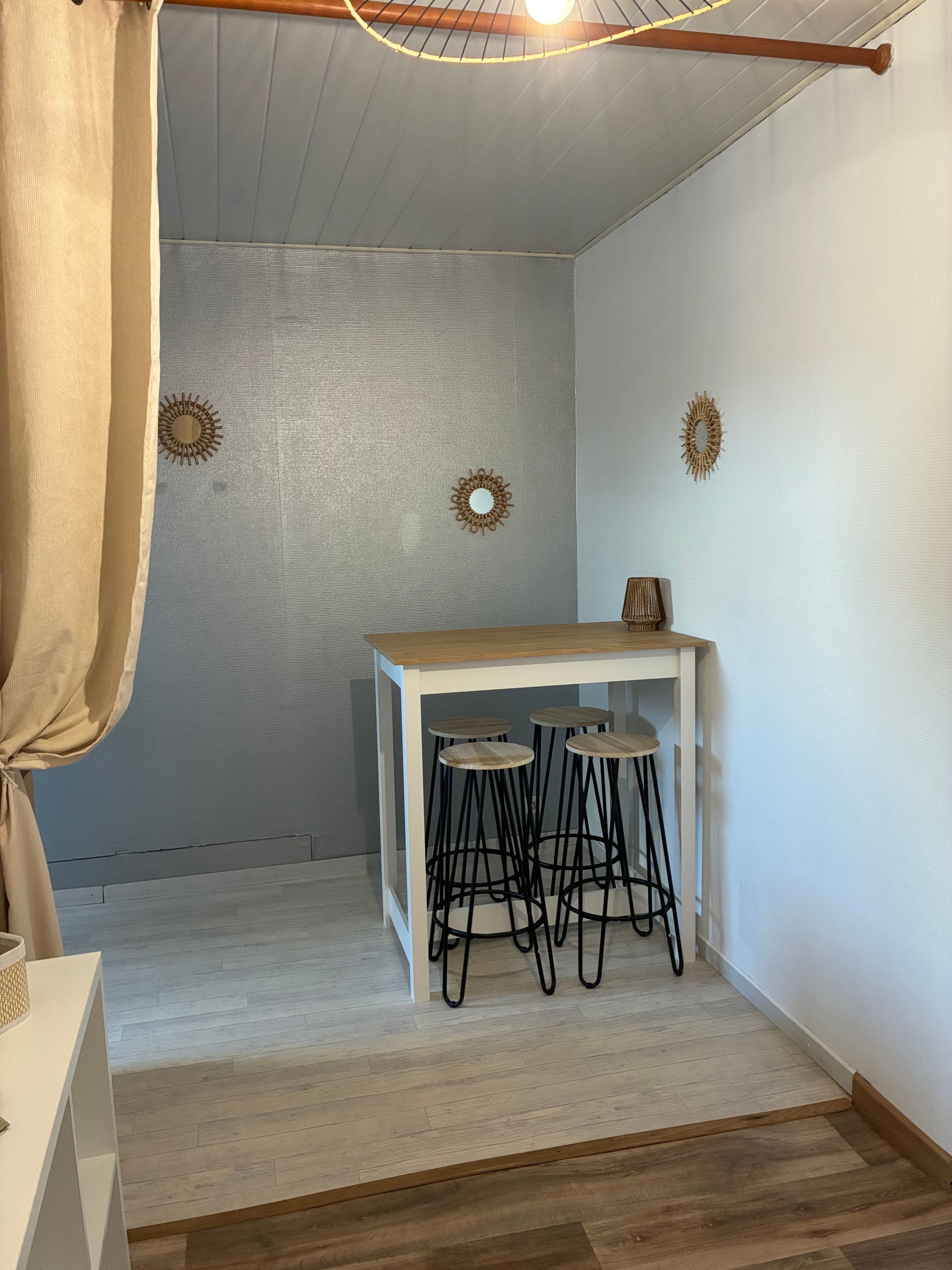 Une petite pièce avec une table blanche et trois tabourets, un luminaire au plafond et deux éléments de décoration murale.