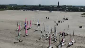 Une vaste étendue de sable où sont amarrés de nombreux voiliers, une église visible au loin et un ciel dégagé.