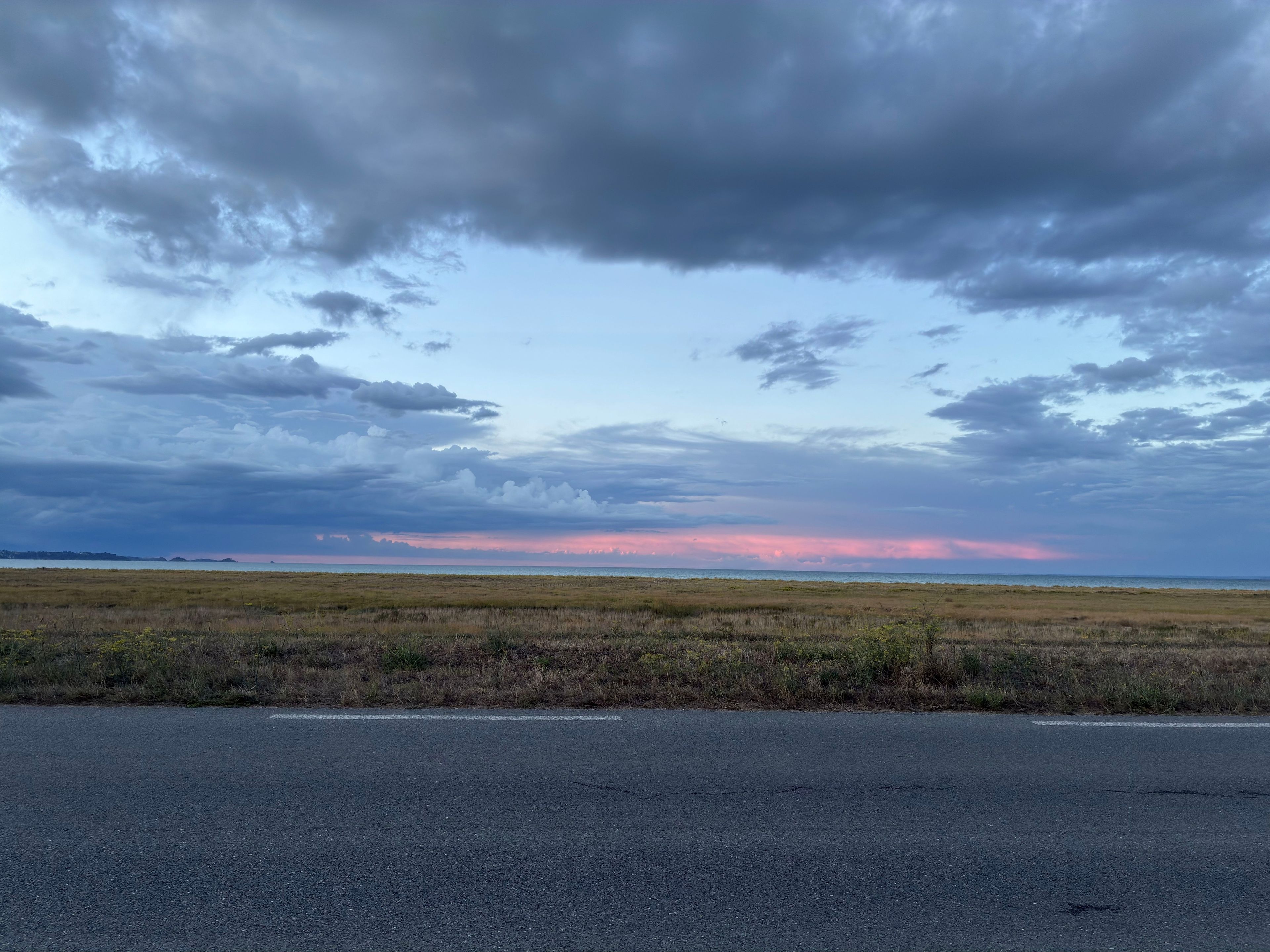 Eine flache Landschaft mit einer Straße im Vordergrund und einem bewölkten Himmel.