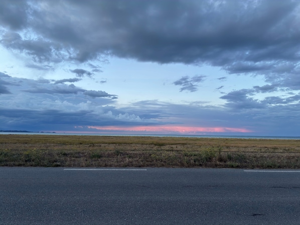 Paisagem plana com estrada em primeiro plano e céu nublado acima.