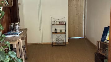 Ein Zimmer mit Holzboden, weißer Decke, einem Regal mit Büchern und Gläsern, einer Pflanze und einer Tür zu einem anderen Raum.