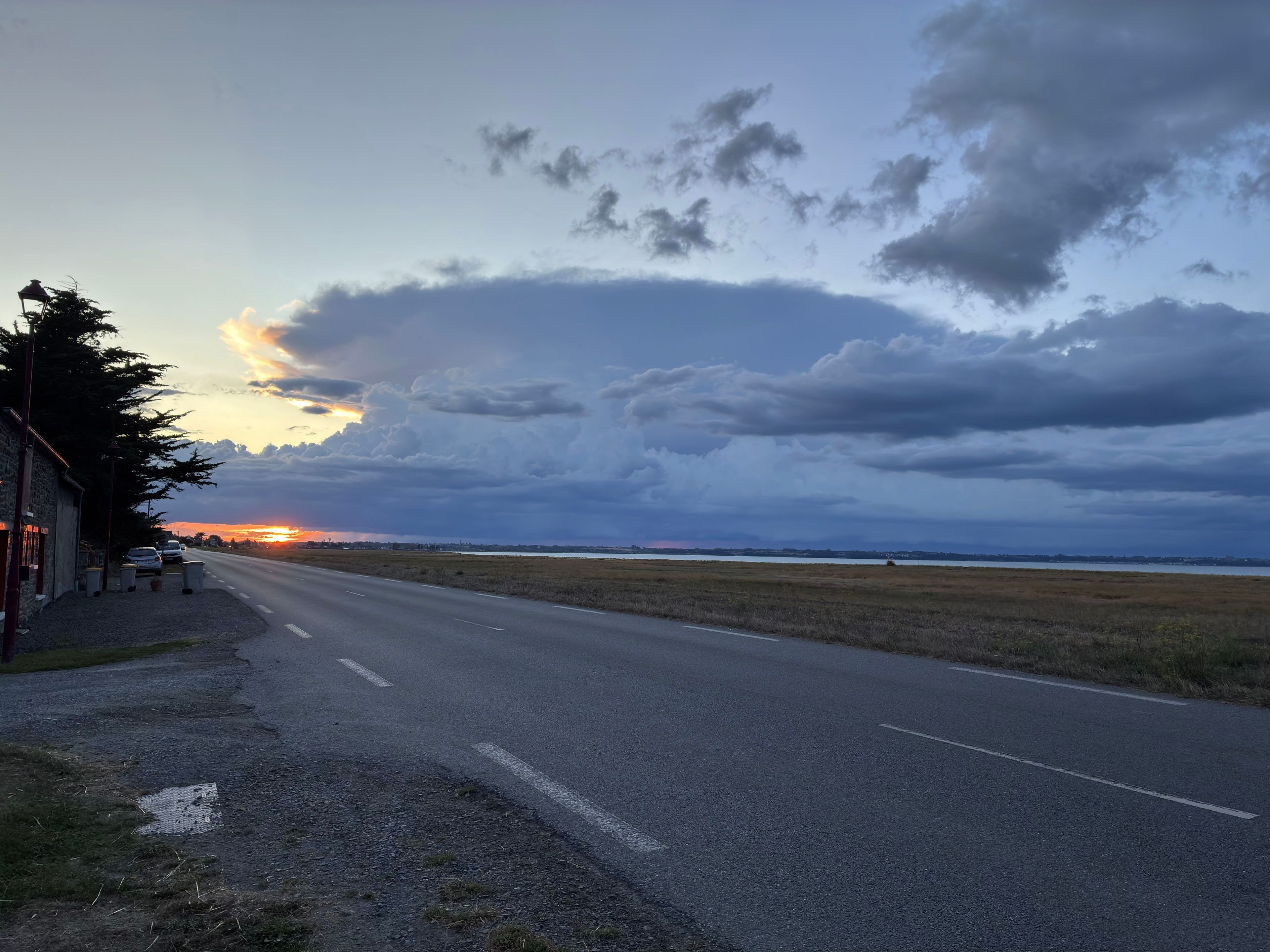 Une route, avec un bâtiment sur la gauche et une étendue d’eau au loin.