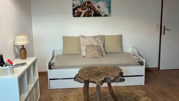 Une chambre à coucher avec un lit, une table basse en bois, une lampe fixée au mur, une étagère avec divers objets et un tableau représentant un voilier.