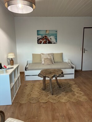 Une chambre à coucher avec un lit, une table basse en bois, une lampe fixée au mur, une étagère avec divers objets et un tableau représentant un voilier.