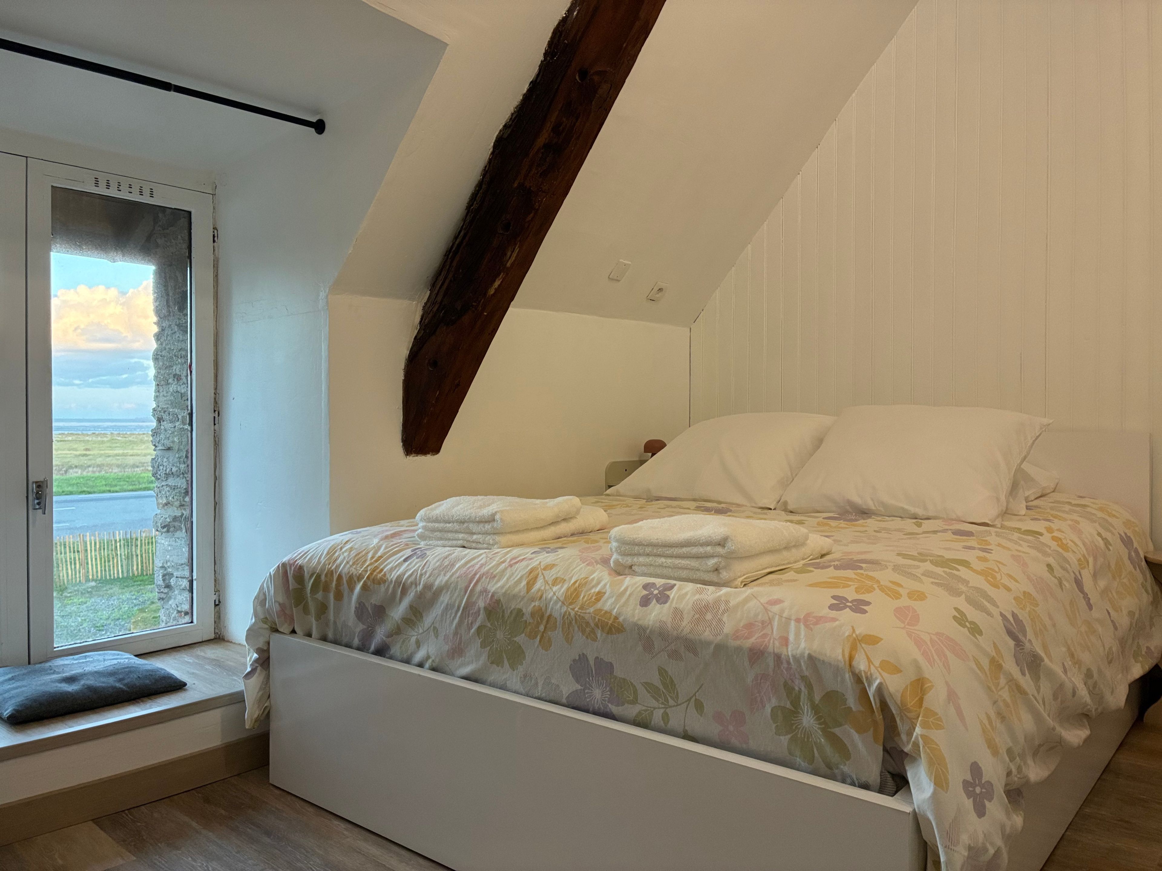 Une chambre à coucher avec un lit, des oreillers, une fenêtre et une vue sur l’extérieur.