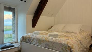 Une chambre à coucher avec un lit, des oreillers, une fenêtre et une vue sur l’extérieur.