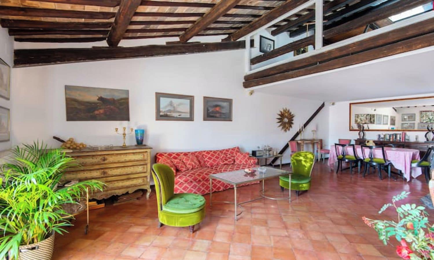 A spacious living area with a high ceiling, a wooden staircase, a dining area with a table and chairs, and a sofa.
