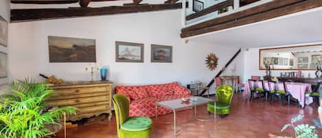 A spacious living area with a high ceiling, a wooden staircase, a dining area with a table and chairs, and a sofa.