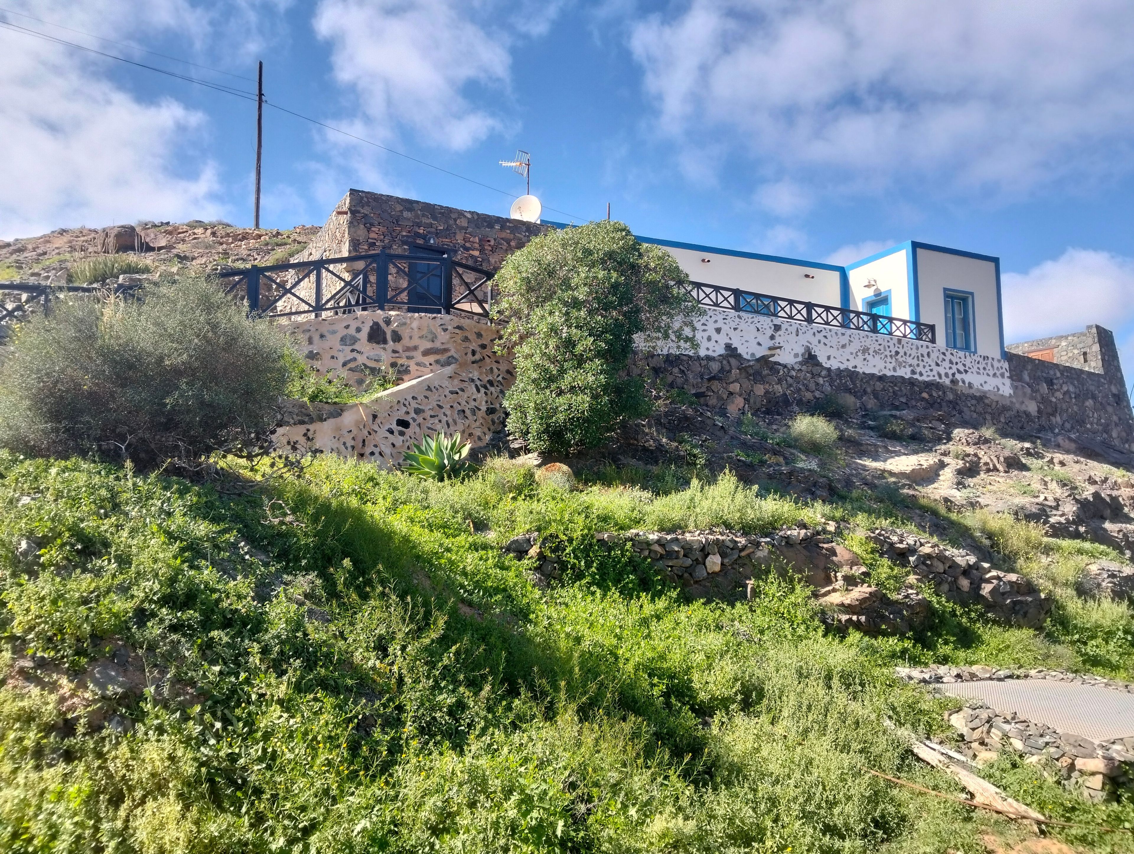 Un bâtiment en pierre, doté d’une antenne parabolique et d’une structure bleue et blanche, situé sur une colline.