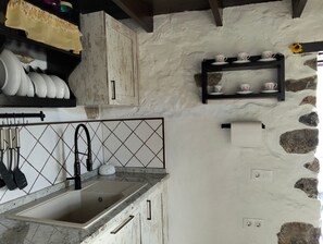 Een keuken met een spoelbak, een betegelde achterwand en een stenen muur.