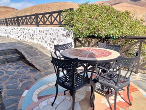 Een terras met een mozaiektafel en stoelen, een stenen muur en uitzicht op heuvels.