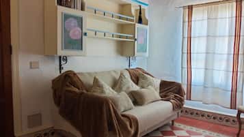 Ein Wohnzimmer mit einer Couch, einem Bücherregal und einem Fenster mit Vorhängen.