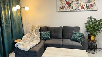 A modern living room with a sectional sofa, a coffee table, a potted plant, and a decorative wall piece.