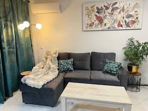 Ein modernes Wohnzimmer mit einer Eckcouch, einem Couchtisch, einer Topfpflanze und einer Wanddekoration.