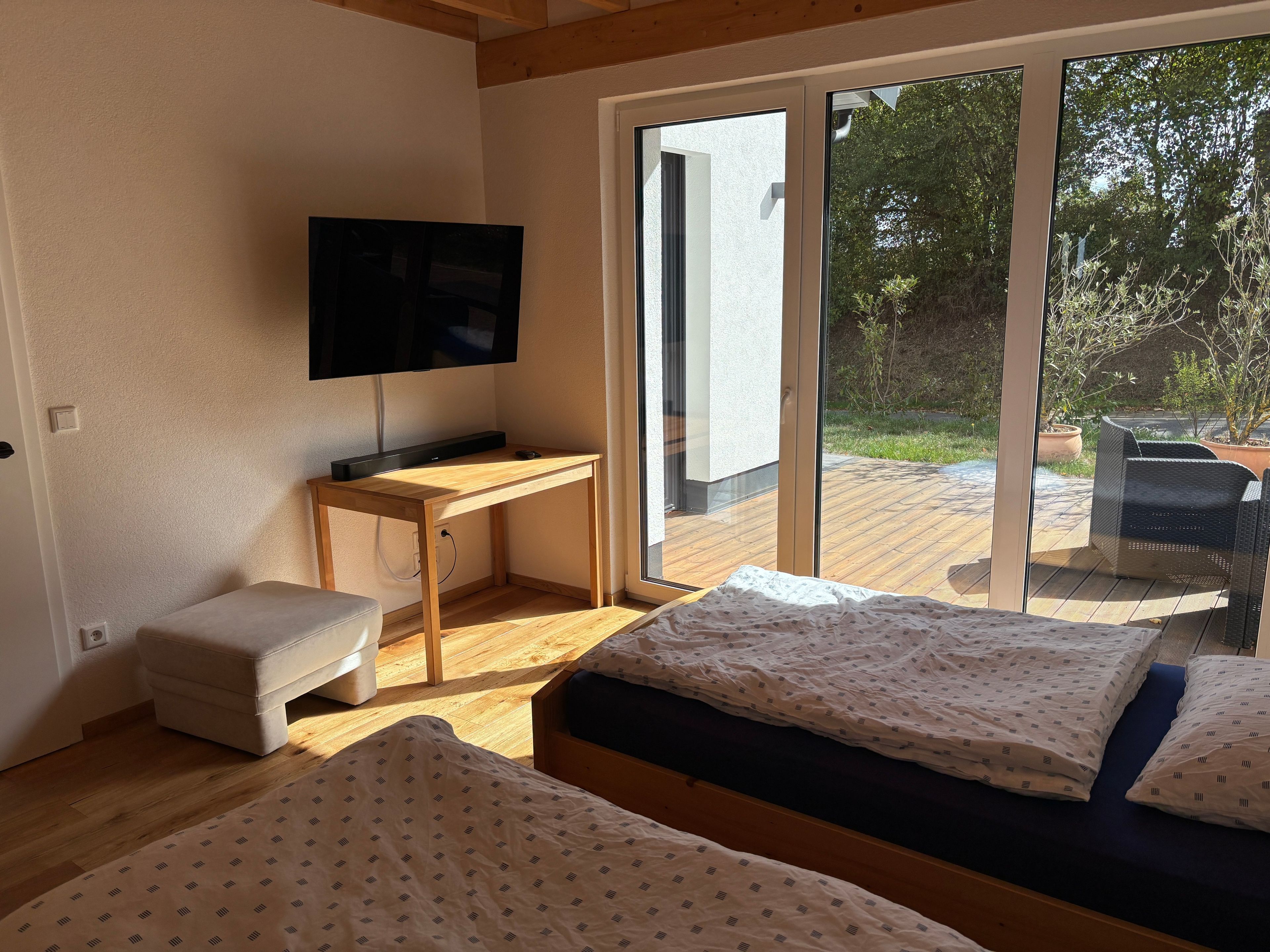 A room with a bed, a desk, a television, and a sliding glass door leading to an outdoor area with a patio.
