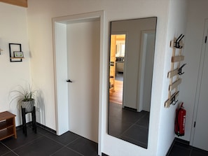 A hallway with a white door, a mirror, a potted plant, a wooden shelf, and a fire extinguisher. - Holiday Home 'Ferienhaus Thomes' in Hunsrück (Külz (Hunsrück))