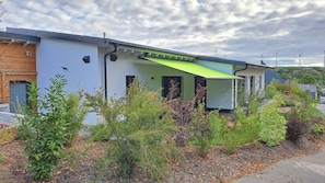 A modern building with a flat roof, a green awning, and a brick section on the left. - Holiday Home 'Ferienhaus Thomes' in Hunsrück (Külz (Hunsrück))