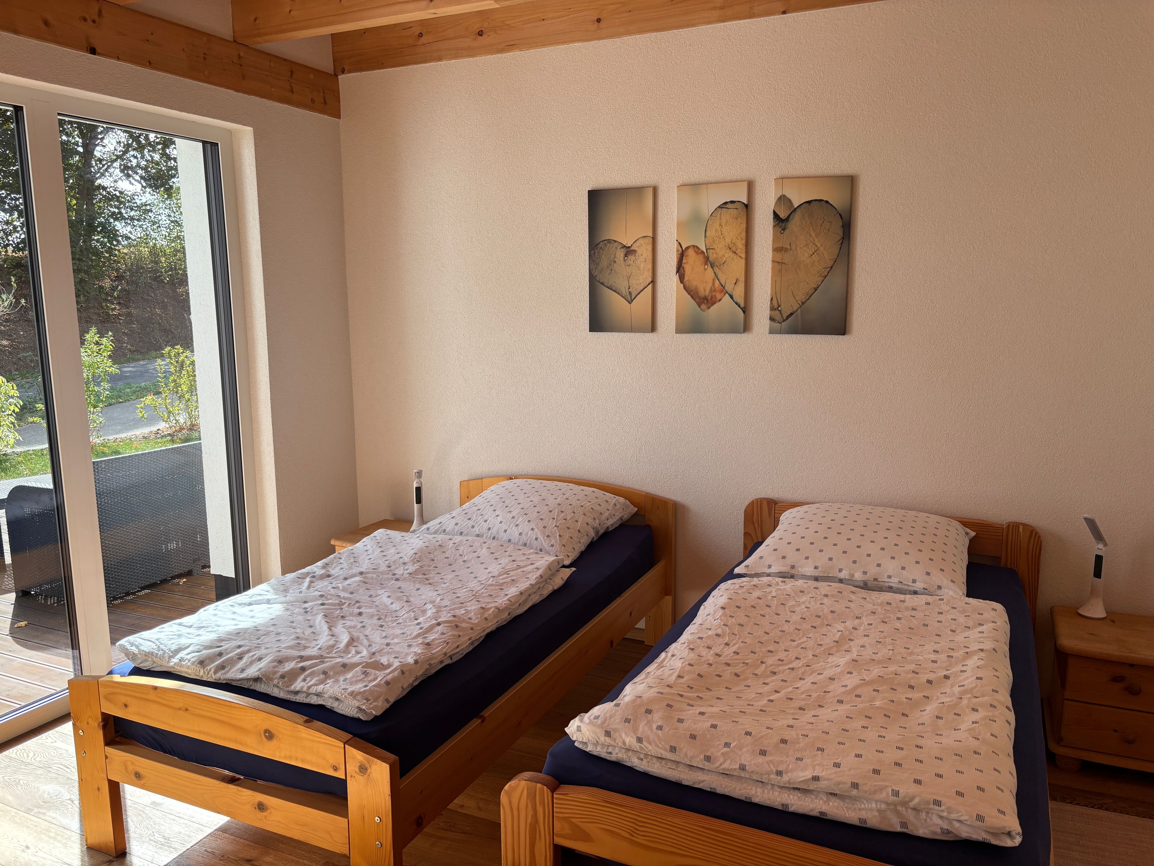 Ein Zimmer mit zwei Holzbettgestellen, einer Schiebetür zu einem Außenbereich und drei an der Wand befestigten Kunstwerken.