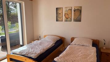 Ein Zimmer mit zwei Holzbettgestellen, einer Schiebetür zu einem Außenbereich und drei an der Wand befestigten Kunstwerken.