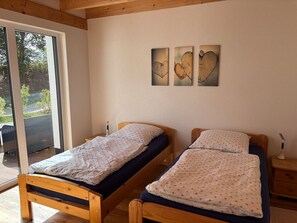 Una habitació amb dos llits de fusta, una porta corredissa de vidre que dona a una zona exterior i tres quadres penjats a la paret.
