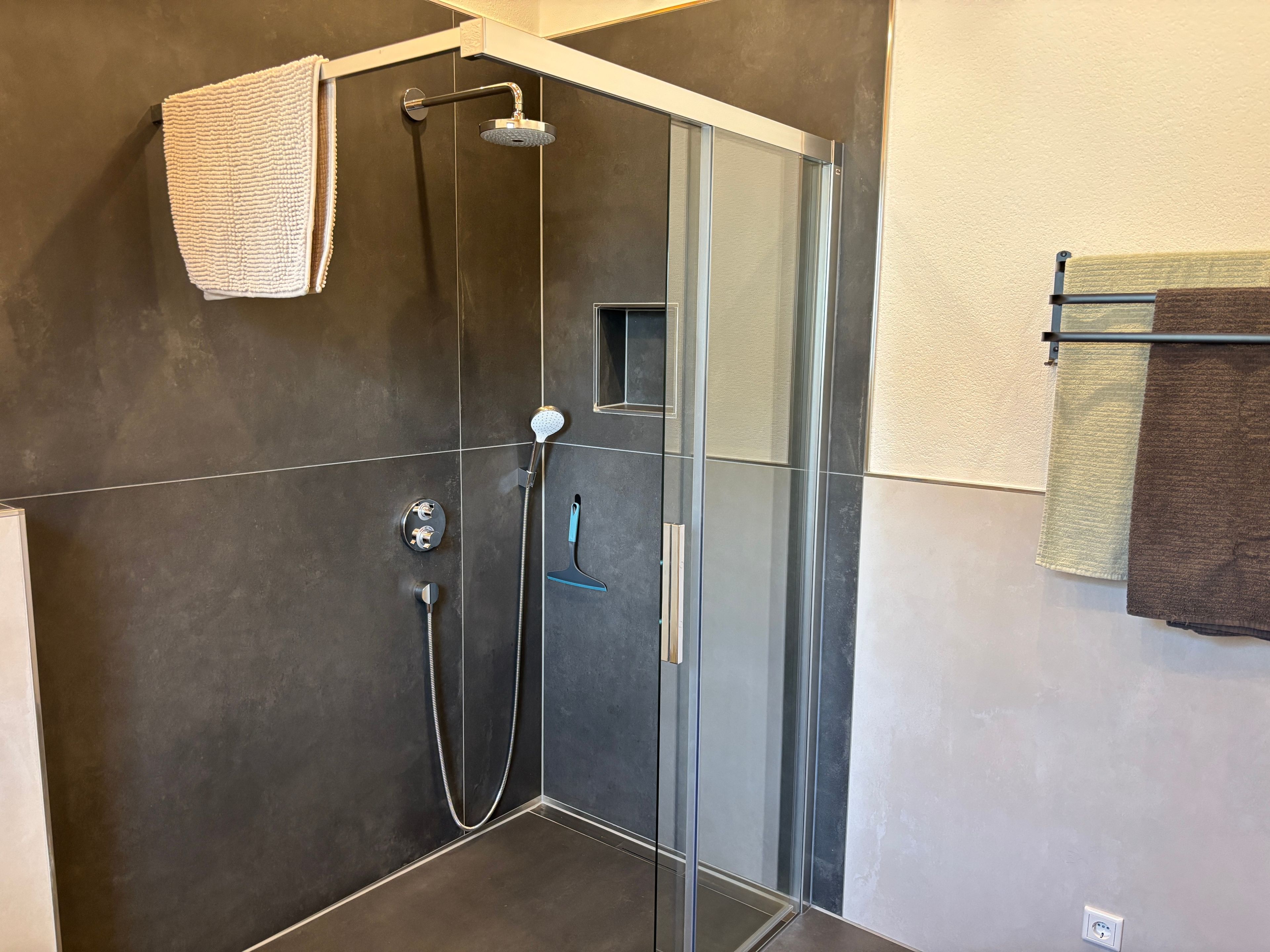 Eine moderne Dusche mit Glastür, einer Handbrause und einem wandmontierten Handtuchhalter.
